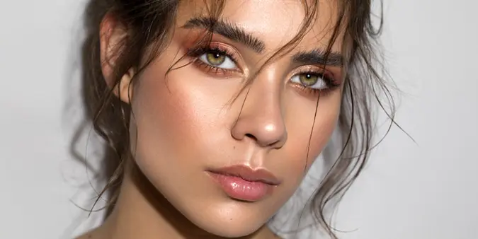 Frau mit professionellem Make-up, betonten Augen, glänzenden Lippen und geformten Augenbrauen – ideal für typgerechte Make-up-Behandlungen.